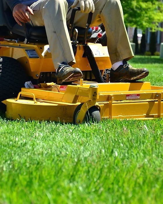 A person operates a yellow ride-on lawnmower, trimming green grass in a sunny outdoor setting. Their focus is on maintaining the landscape.