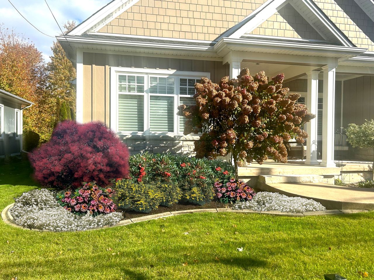 A house with a manicured front yard featuring vibrant flowers and bushes, clear windows, and a well-maintained grass lawn under sunny skies.